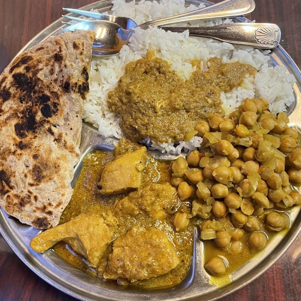 A Tibet Kitchen thali with rice, chicken curry, chickpea curry, and flatbread on a metal plate.