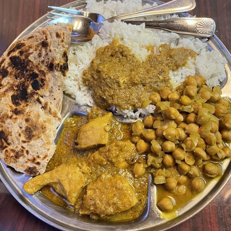 A Tibet Kitchen thali with rice, chicken curry, chickpea curry, and flatbread on a metal plate.
