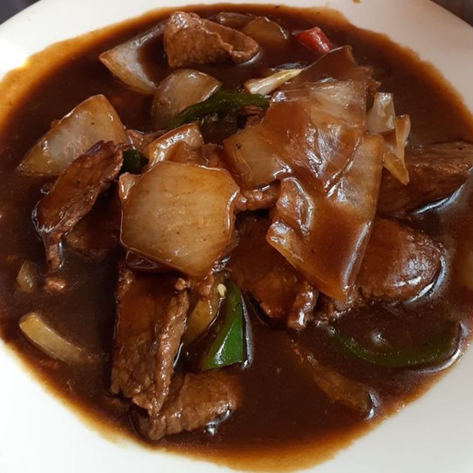 Tibet Kitchen's beef and onion dish in a rich brown sauce, served in a white bowl.
