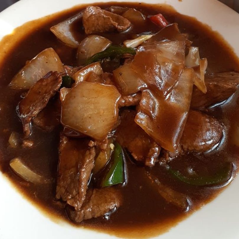 Tibet Kitchen's beef and onion dish in a rich brown sauce, served in a white bowl.